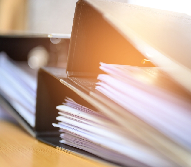 資料の挟まった複数のバインダーが積み重なっている画像